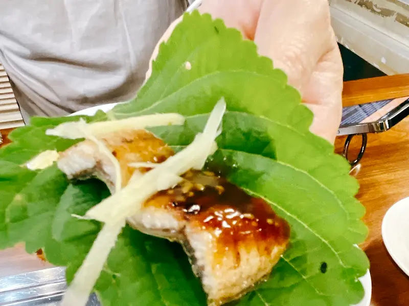 깻잎에 장어와 생강채를 올려 쌈을 싸 먹는 모습