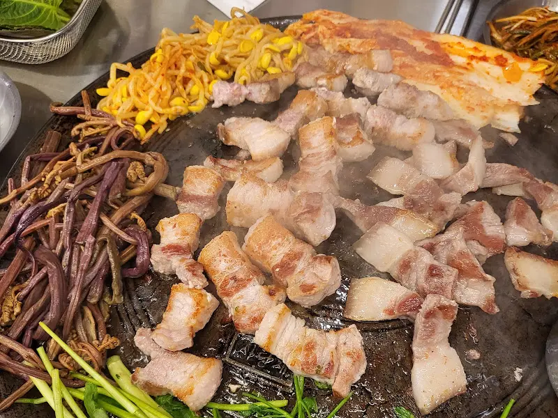 솥뚜껑 위에 올려진 꼬들목살과 다양한 곁들임 채소들