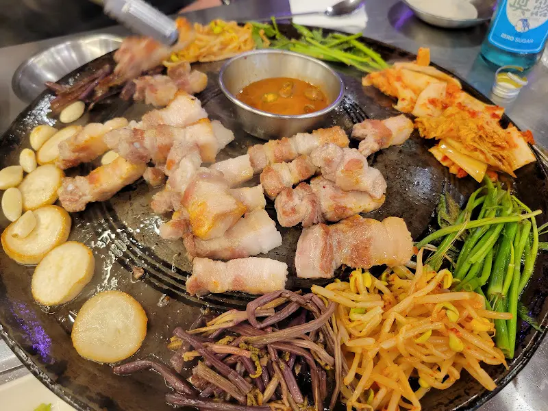 다양한 곁들임 채소와 함께 솥뚜껑에 구워진 꼬들목살