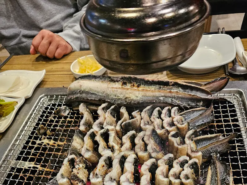 숯불 위에 구워지는 장어와 다양한 밑반찬