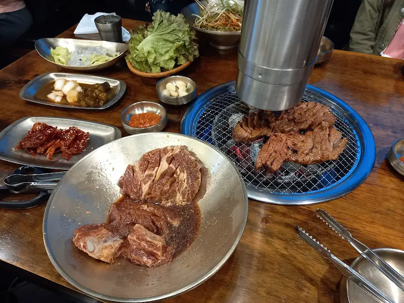 숯불 위에서 맛있게 익어가는 돼지갈비와 푸짐한 밑반찬