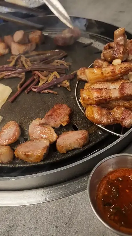 불판 위에서 익어가는 삼겹살과 곁들임 채소