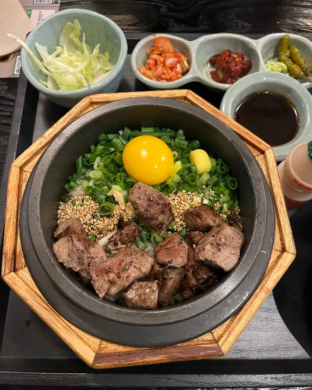 스테이크 솥밥의 클로즈업 샷, 윤기가 흐르는 스테이크와 밥알이 인상적이다.