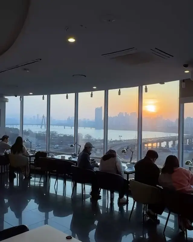 넓은 창가 좌석에서 석양을 바라보며 식사하는 손님들의 모습