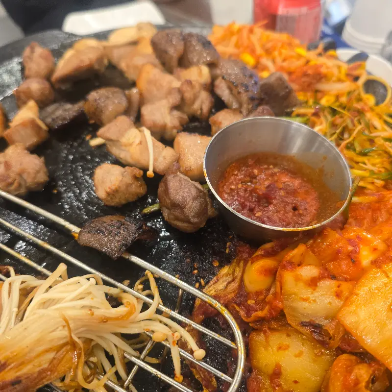 불판 위에 가득 찬 뒷고기와 곁들임 채소