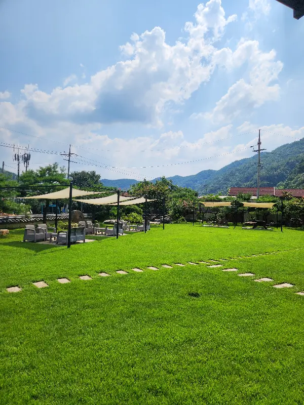 푸른 잔디밭 위에 놓인 테이블과 의자. 파란 하늘과 뭉게구름이 어우러진 풍경이 그림 같다.