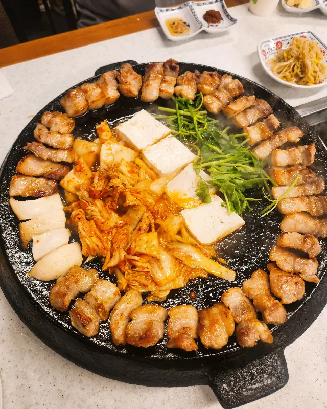 무쇠 불판 가득 채워진 삼겹살과 곁들임 채소