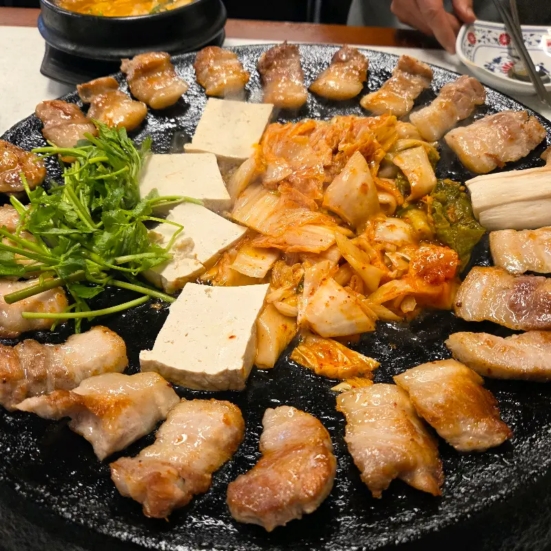 무쇠 불판 위에 가지런히 놓인 삼겹살과 김치, 두부