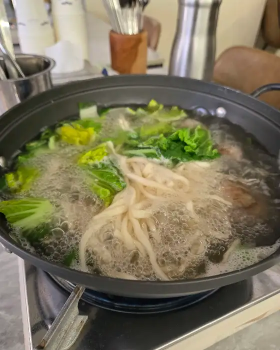 테이블 위에서 끓고 있는 백합 칼국수 냄비. 배추와 면이 보입니다.