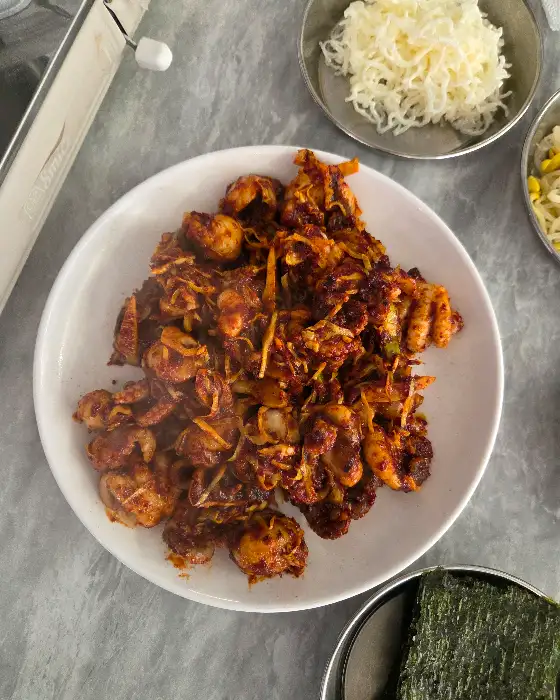 아리찬 쭈꾸미 앞산점의 쭈꾸미볶음 전체 상차림 사진. 쭈꾸미볶음 접시 중앙에 놓여 있고, 주변으로 곤드레밥, 칼국수, 김, 콩나물 등 다양한 반찬이 보입니다.