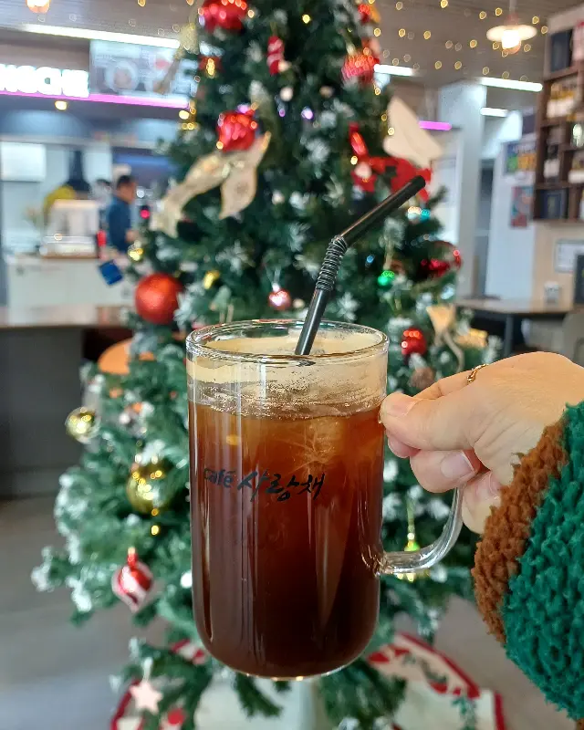 크리스마스 트리 앞에서 찍은 아이스 아메리카노 사진