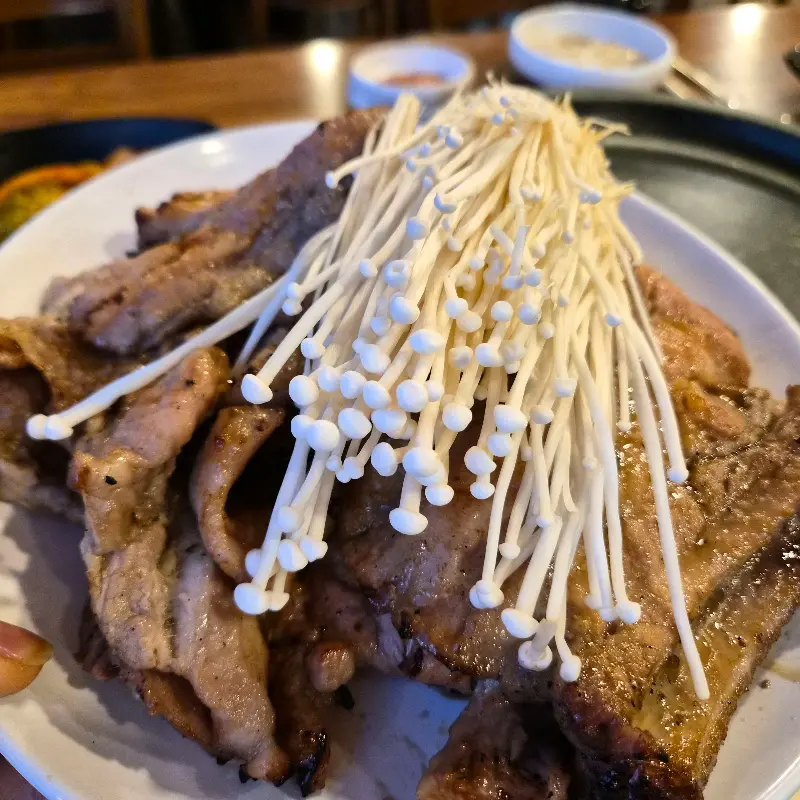 초벌되어 나온 돼지갈비 위에 팽이버섯이 듬뿍 올려져 있다