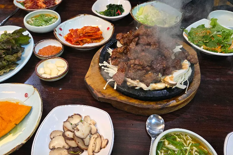 뜨거운 돌판 위에 놓인 돼지 석갈비와 다양한 반찬들의 모습