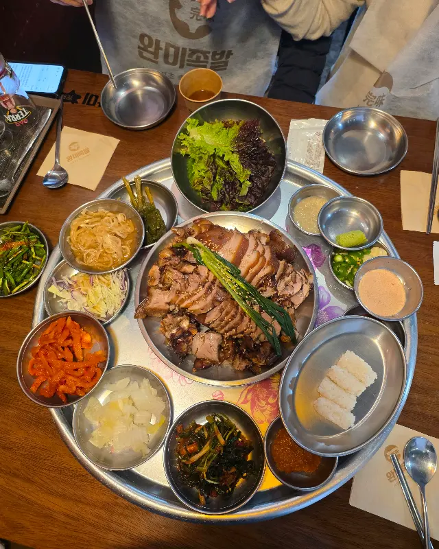 족발, 곁들임 찬, 막걸리가 한 상 가득 차려져 푸짐한 모습을 연출하고 있다.