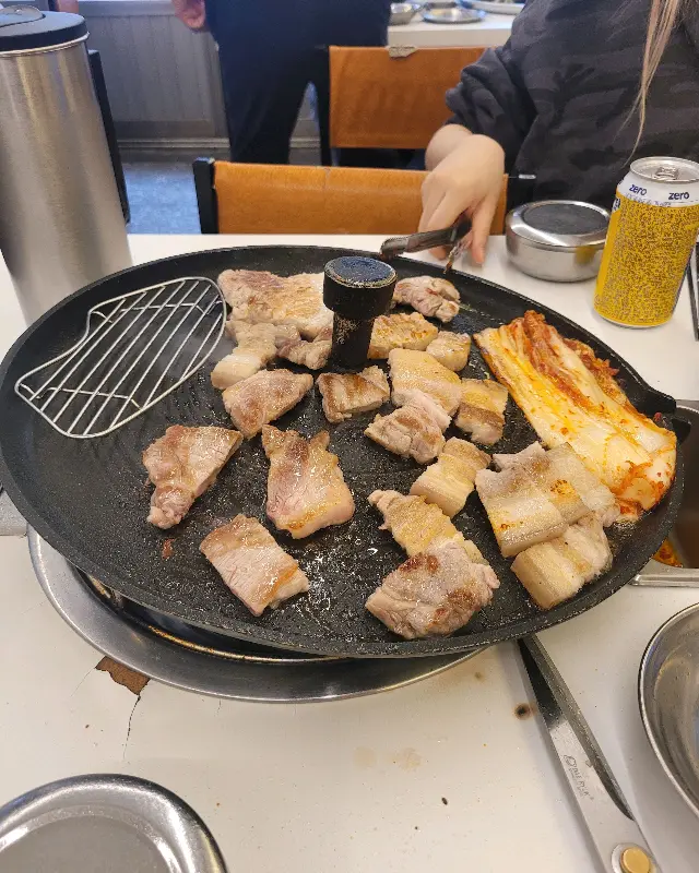 솥뚜껑에 삼겹살과 김치를 구워 먹기 좋게 자르는 모습