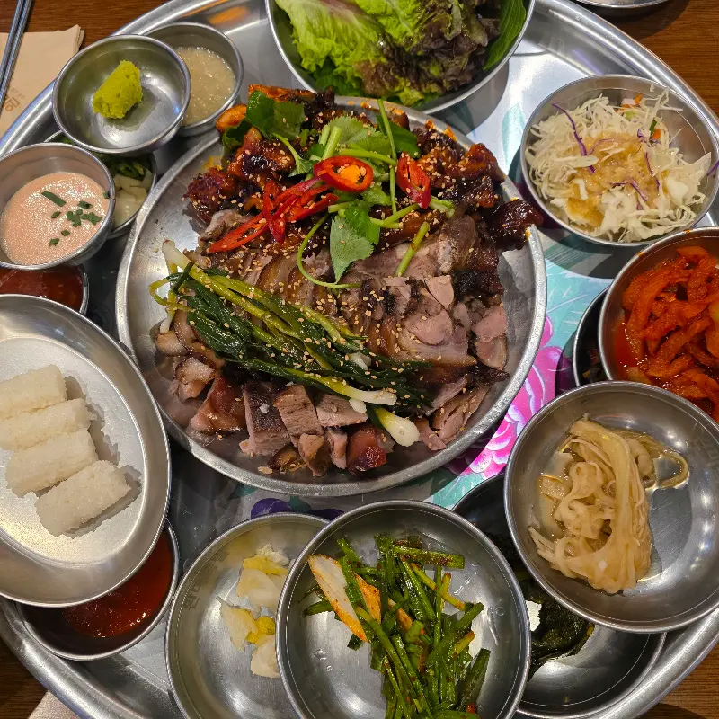 윤기가 흐르는 족발 위에 쪽파가 얹어져 있고, 곁들임 찬들이 쟁반 가득 놓여 있는 모습