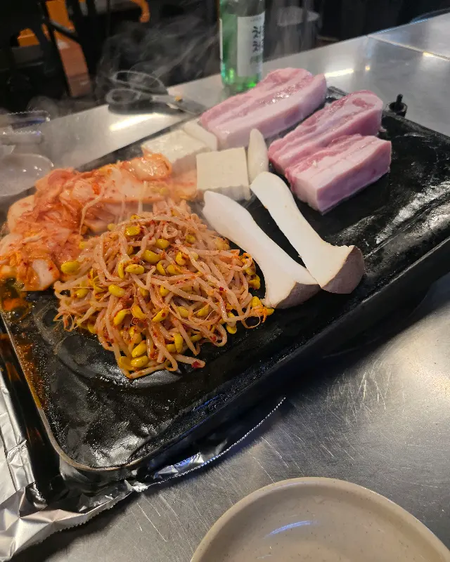 돌판 위에 올려진 두툼한 삼겹살과 김치, 콩나물