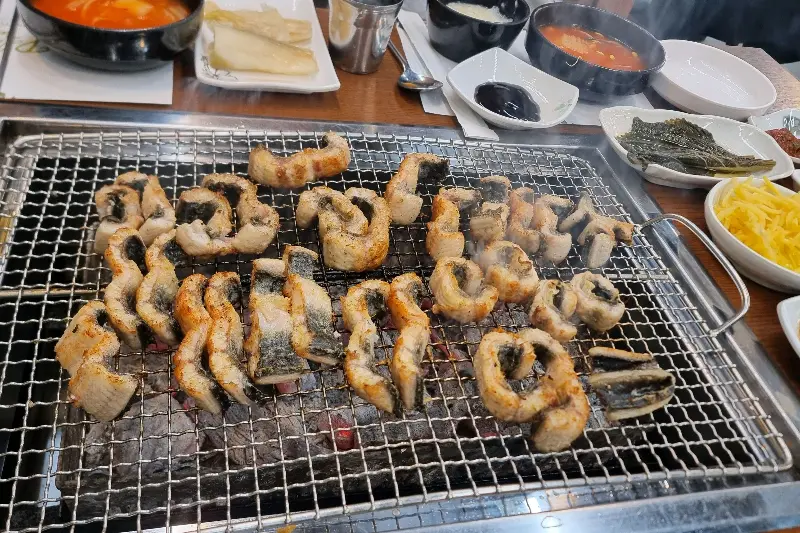 숯불 위에서 맛있게 익어가는 장어와 푸짐한 밑반찬