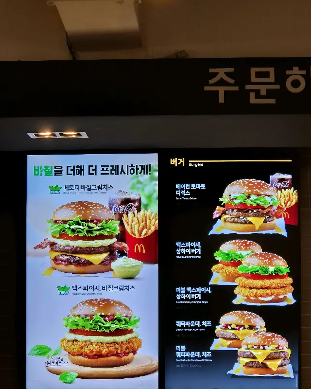디지털 메뉴보드에 맥스파이시 바질크림치즈 버거 세트가 선명하게 보인다.