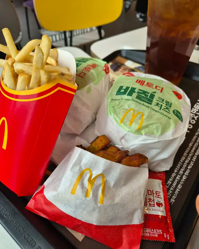 맥스파이시 바질크림치즈 버거, 창녕마늘 스낵랩, 맥윙, 그리고 감자튀김이 테이블 위에 놓여있는 모습