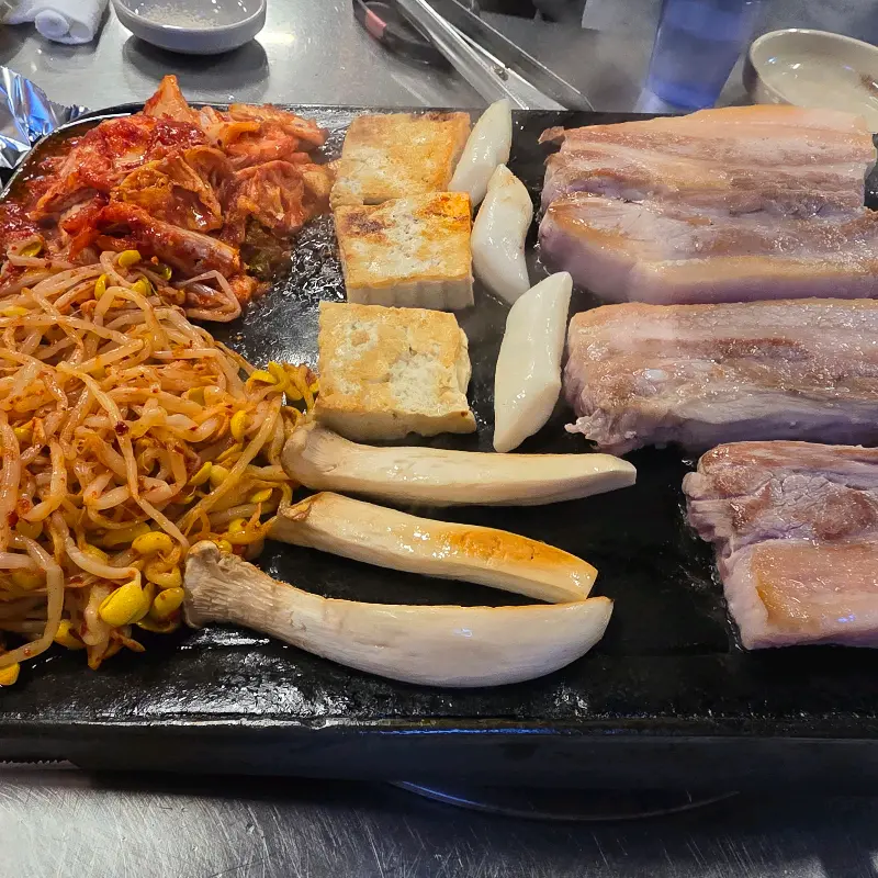 돌판에 구워지는 삼겹살, 김치, 콩나물, 두부