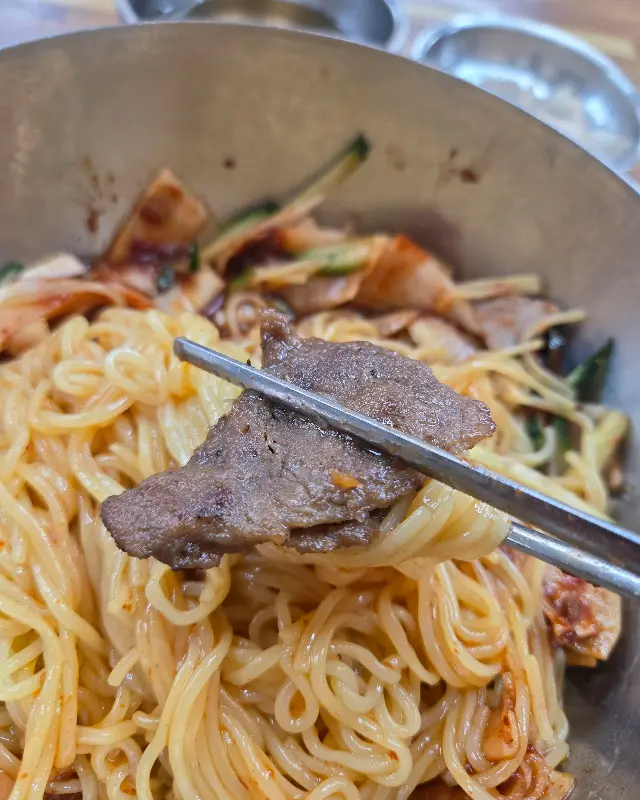 젓가락으로 집어 올린 석쇠불고기와 비빔밀면 면발