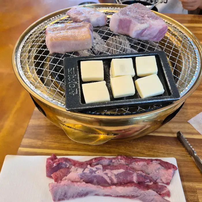 숯불 위에서 구워지는 삼겹살과 목살, 그리고 치즈구이가 함께 준비되어 있습니다.