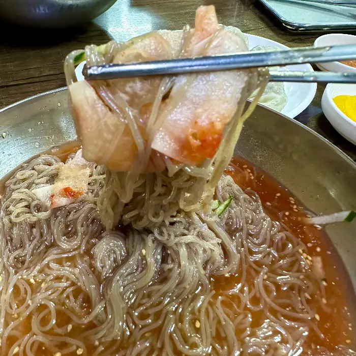 집게로 냉면 고기를 집어 올리는 모습.