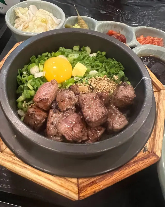 스테이크 솥밥의 클로즈업 샷, 밥 위에 스테이크와 함께 다양한 고명이 올려져 있다.