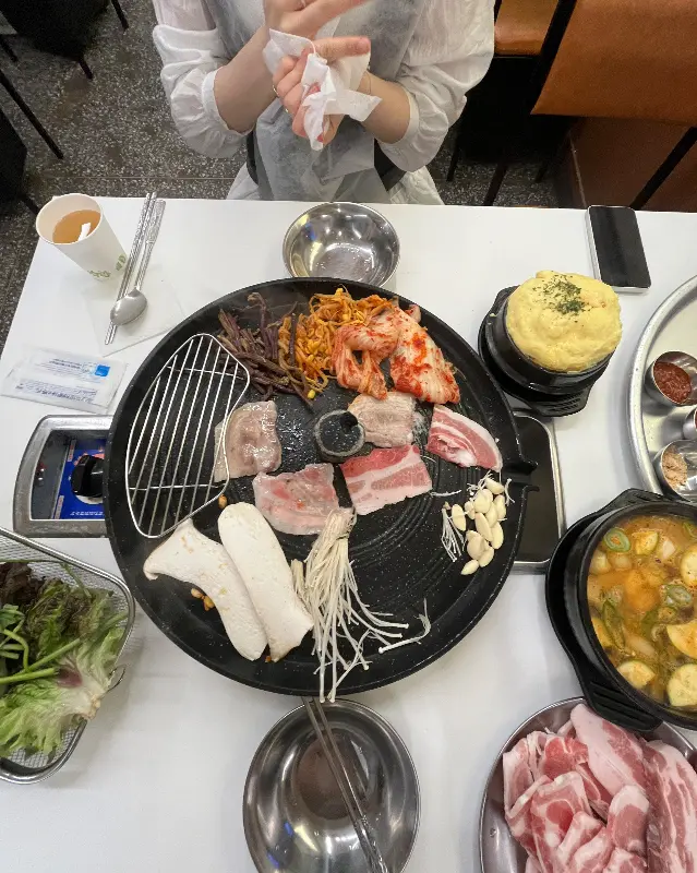 솥뚜껑 위에 삼겹살과 함께 구워진 김치, 콩나물, 버섯