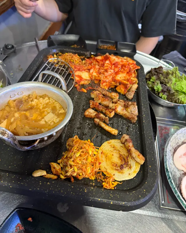 불판 위에 김치, 콩나물과 함께 구워지는 삼겹살