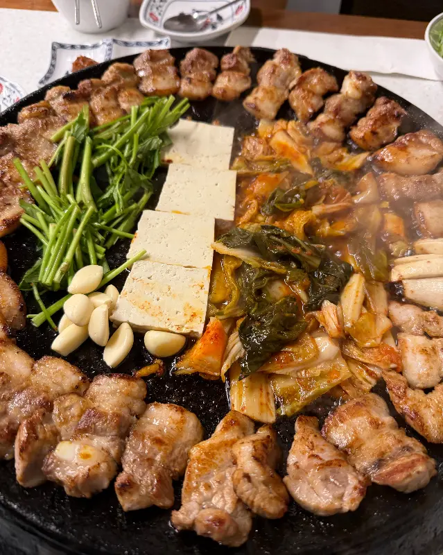 무쇠 불판 위에 삼겹살, 김치, 두부가 함께 구워지는 모습
