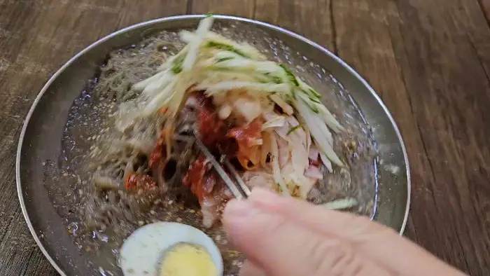 냉면 면발을 집어 올리며 국물을 살짝 묻히는 모습.