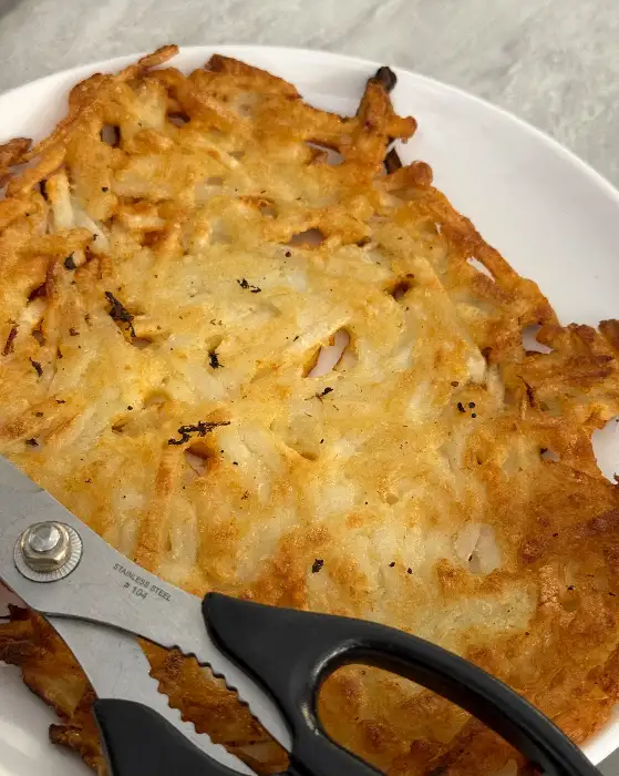 바삭하게 튀겨진 감자전의 클로즈업 사진. 가위가 함께 놓여 있어 먹기 좋은 크기로 자를 준비가 되었음을 보여줍니다.