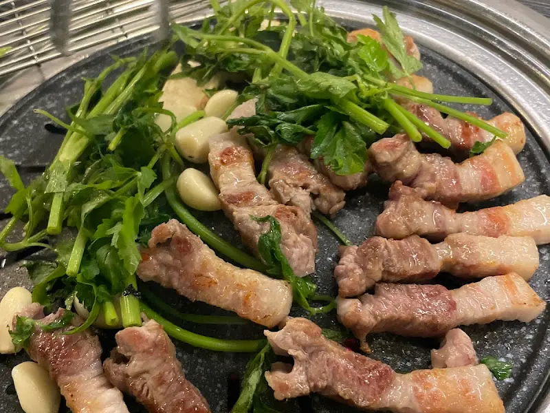 잘 구워진 삼겹살과 미나리, 마늘이 함께 불판 위에 올려져 있는 모습