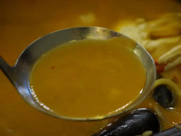 국자를 떠낸 짬뽕 국물의 노란 빛깔이 선명하게 보입니다. 국물 위에는 약간의 고춧가루가 떠 있습니다.