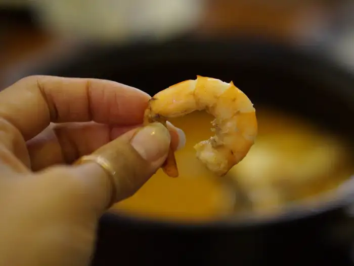 손가락에 집힌 작고 통통한 새우 한 마리가 클로즈업되어 있습니다. 새우는 핑크빛을 띠며 탱글탱글해 보입니다.