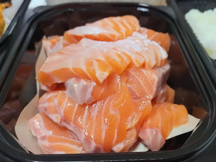 신선한 연어회가 산더미처럼 쌓여 있습니다. 선홍빛 연어와 흰 지방층이 대비를 이루며 먹음직스럽습니다.