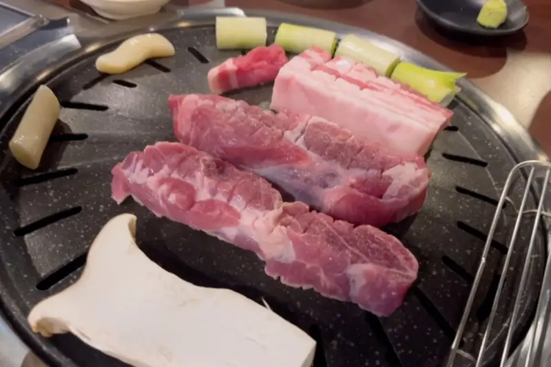 불판 위에 올려진 삼겹살과 버섯, 떡