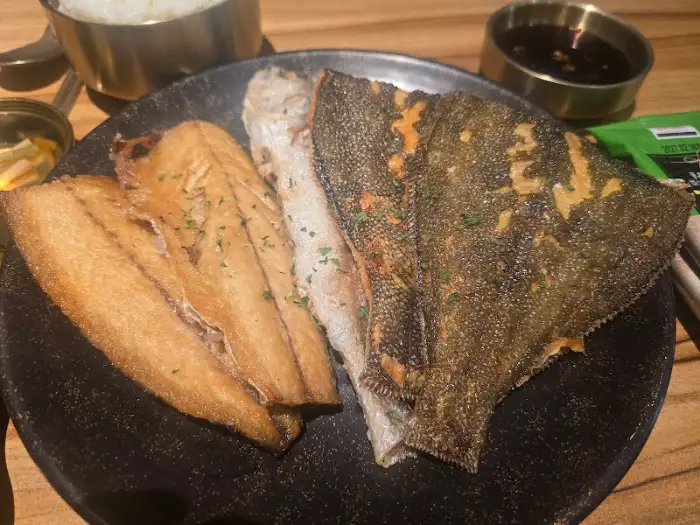 노릇하게 구워진 생선 한 토막과 묵직한 검은 접시가 보입니다.
