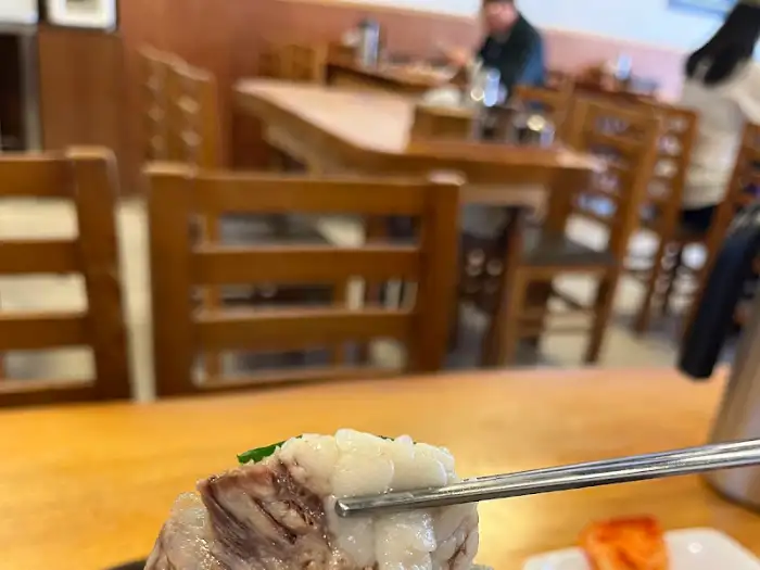 한우장 내부 테이블 풍경. 나무 테이블과 의자로 이루어진 편안한 분위기 속에서 사람들이 식사하고 있다.