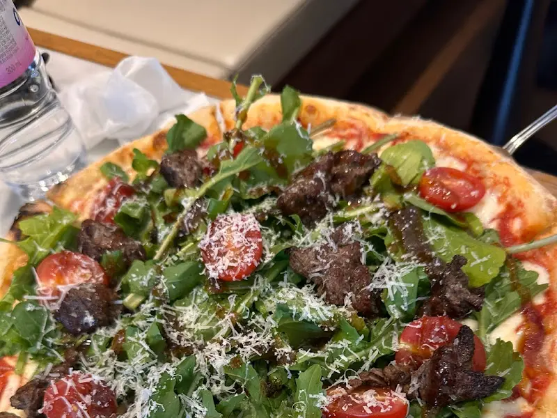 스테이크 피자의 압도적인 비주얼, 육즙 가득한 스테이크와 신선한 루꼴라가 조화롭다.
