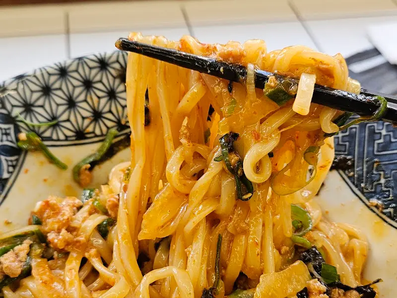 젓가락으로 카제소바 면을 들어올린 모습. 윤기가 흐르는 면발과 매콤한 양념이 조화롭게 어우러져 있다.