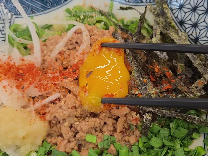 젓가락으로 카제소바를 집어 올린 모습. 가운데 노른자가 얹혀져 있고, 김가루와 다진 고기가 함께 보인다.