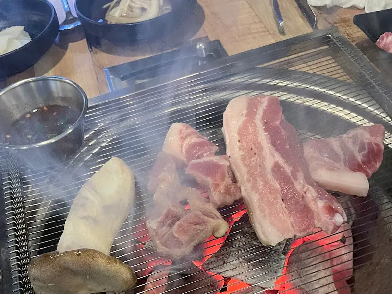 숯불 위에서 연기를 내며 익어가는 삼겹살과 꼬들목살