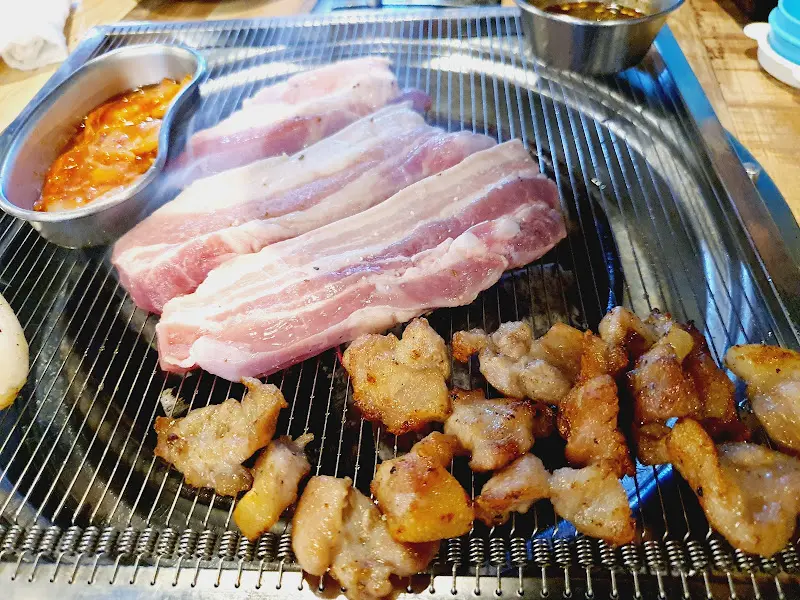 숯불 위에서 삼겹살과 꼬들목살이 익어가는 모습, 젓갈이 함께 보인다.