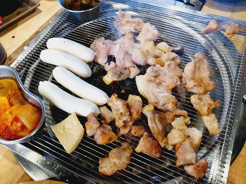 불판 위에 꼬들목살, 버섯, 떡, 김치가 함께 구워지는 모습