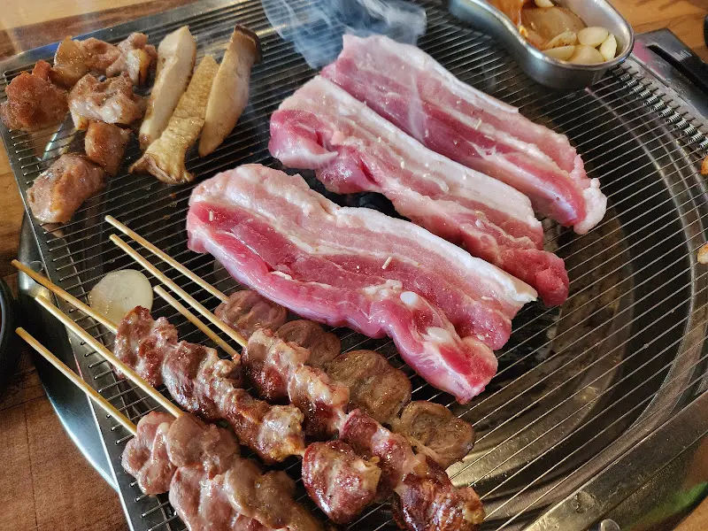 불판 위에서 삼겹살과 염통꼬치가 함께 구워지는 모습