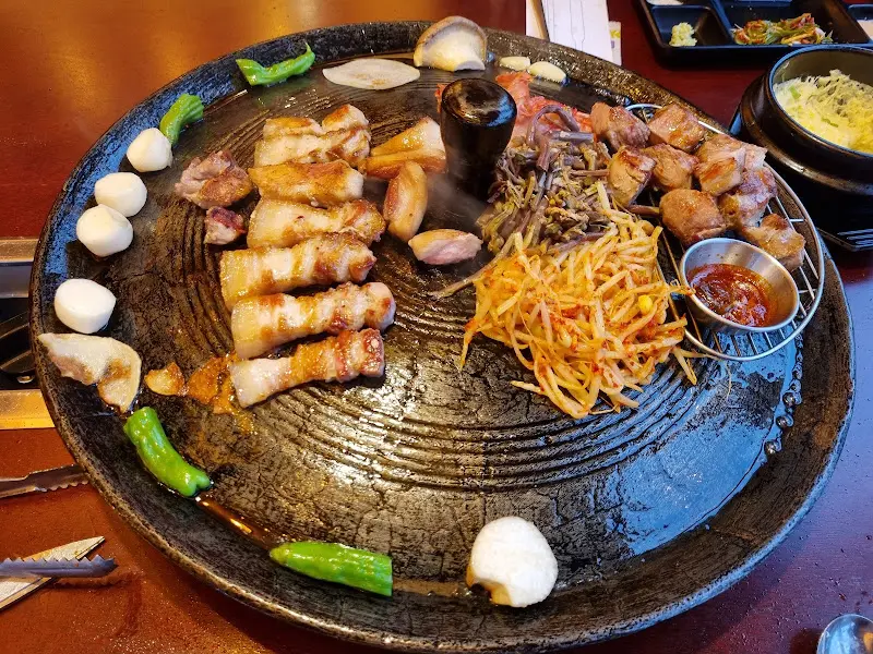 솥뚜껑 위에 목살, 고사리, 콩나물, 김치가 함께 구워지고 있는 모습