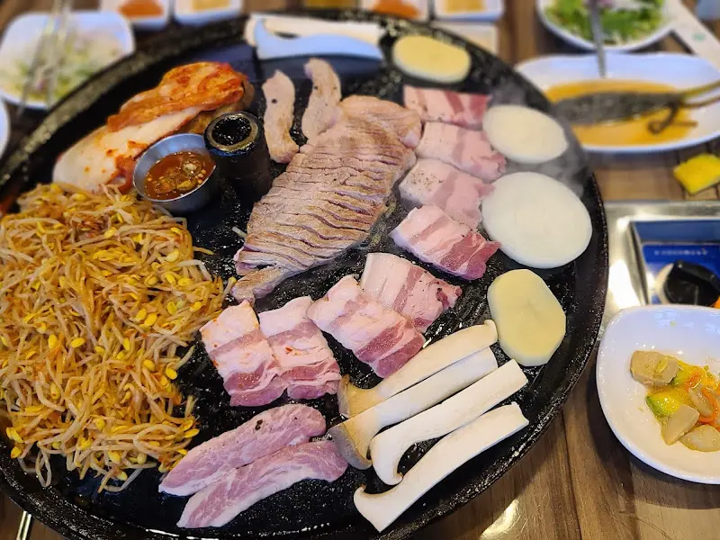 솥뚜껑 가득 차려진 삼겹살과 밑반찬